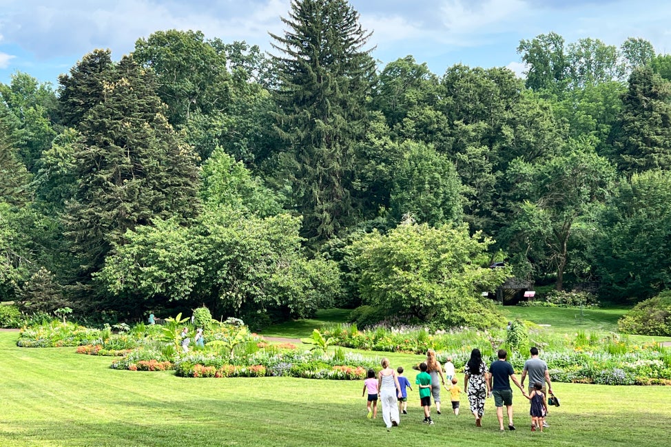 A landscape view of a public garden with families walking through a field toward paisley-shaped garden beds in blooms. 