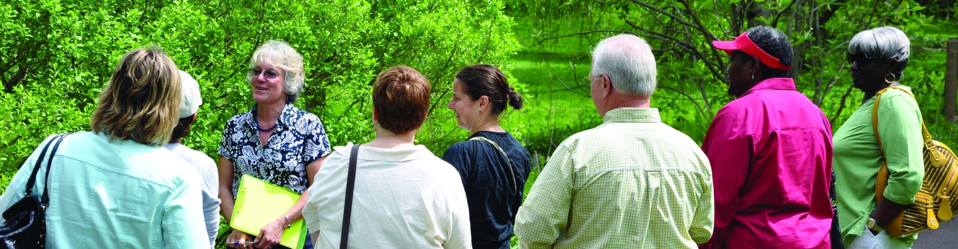 A group of people on a garden tour with bright green trees in the background.