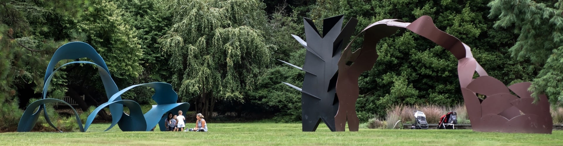 A small family sitting under a looping blue and red looping sculpture on the grass. 