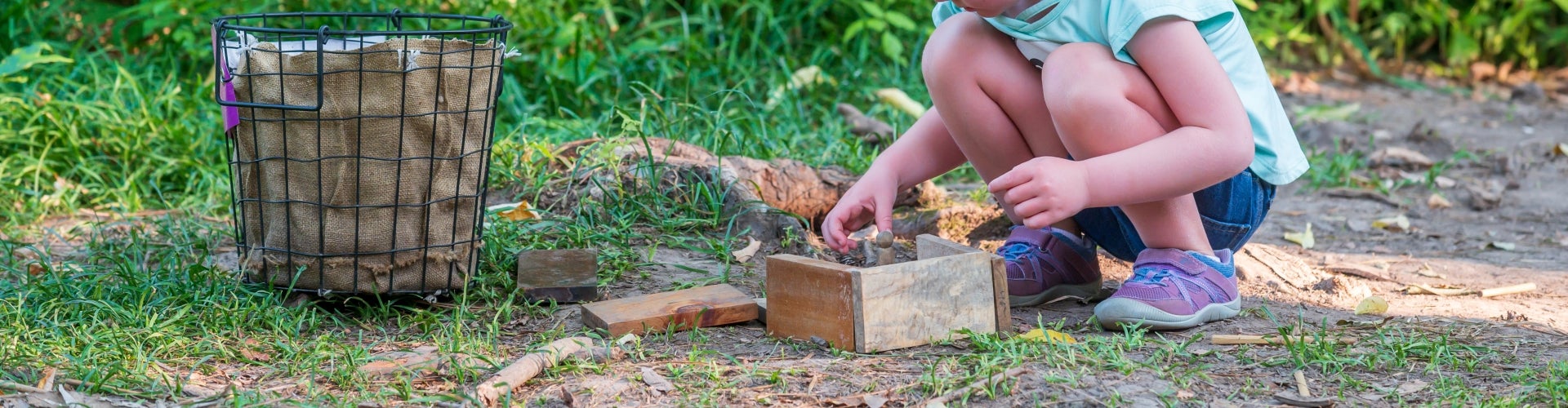 A young girl builds a fairy house out of natural materials outdoors.