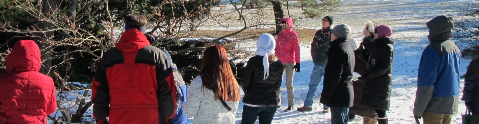 A group of people wearing winter coats taking a public garden tour in the snow.