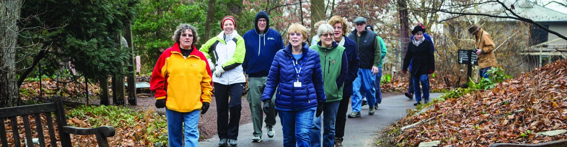 A group of people wearing winter coats walk along a paved wooded path.