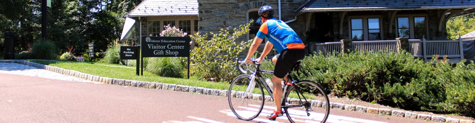 A cyclist rides along a paved path toward a sign that reads, "Visitor Center."