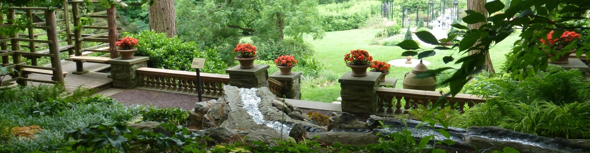 A stone walkway with planters filled with orange flowers, surrounded by greenery. 