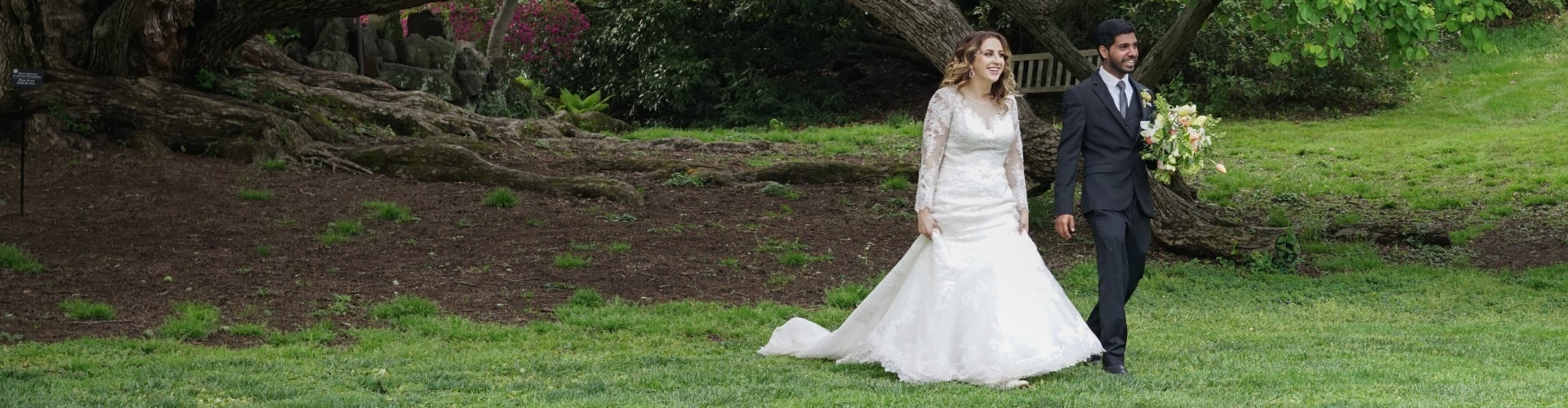 A bride and groom walk along a green, outdoor landscape.