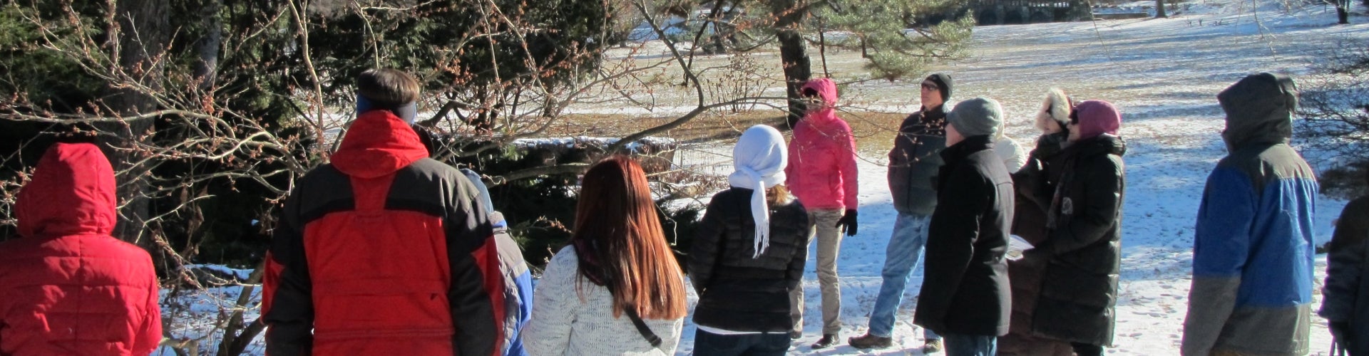 A group of people in winter coats take a tour of a snowy public garden on a sunny day. 