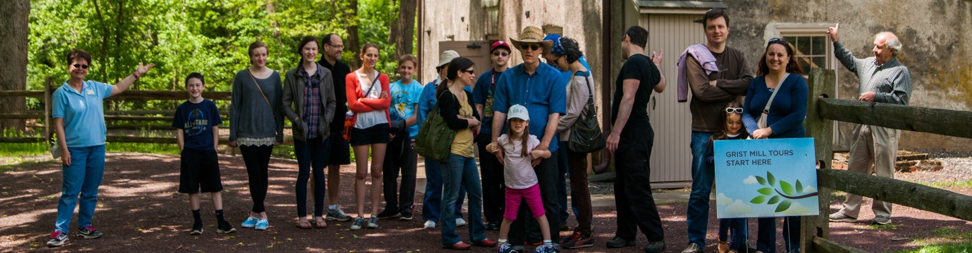 A group of people smile at the camera while standing in line to take a tour of a historic mill. 