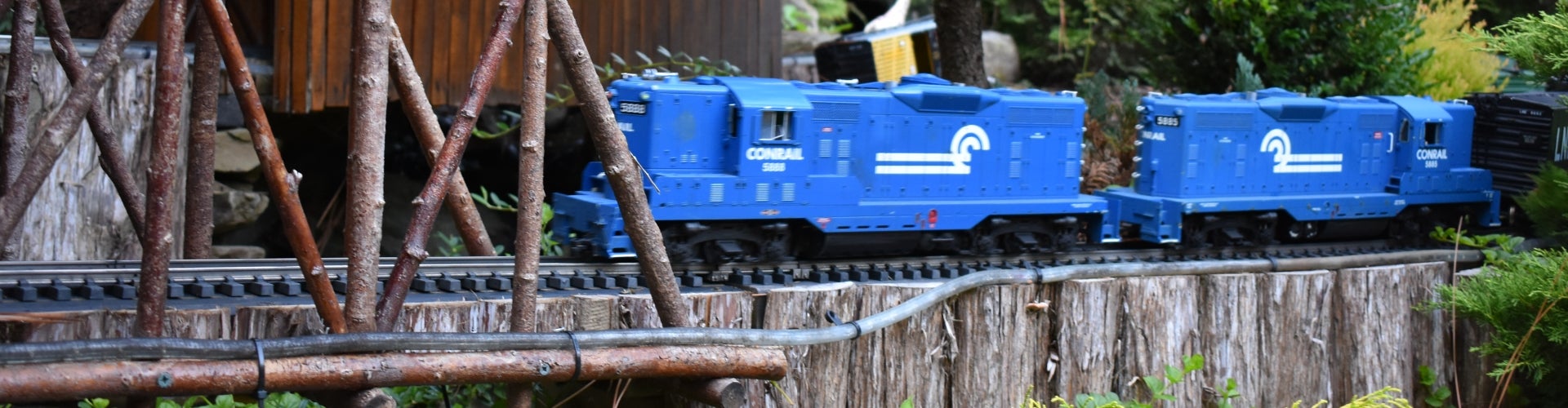 A blue model train rides through a wooden trestle. 