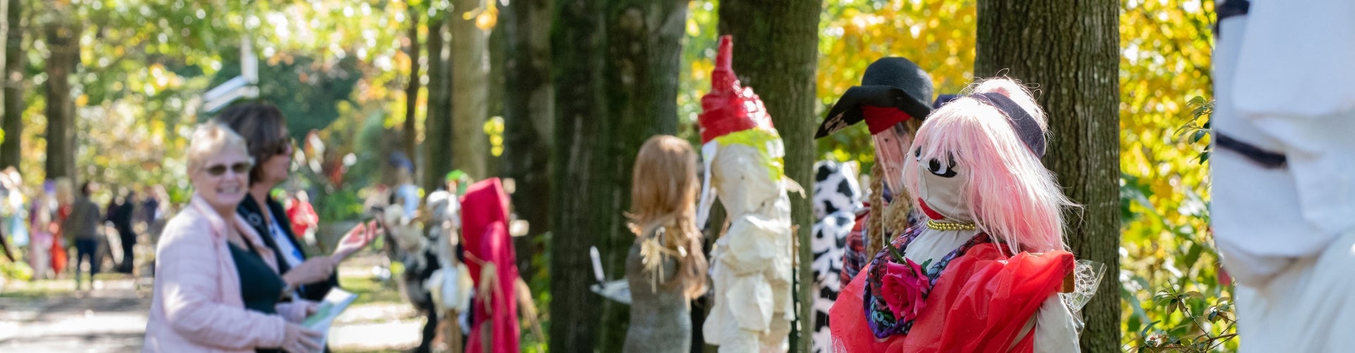 A group of women smile while looking at scarecrows in a public garden.