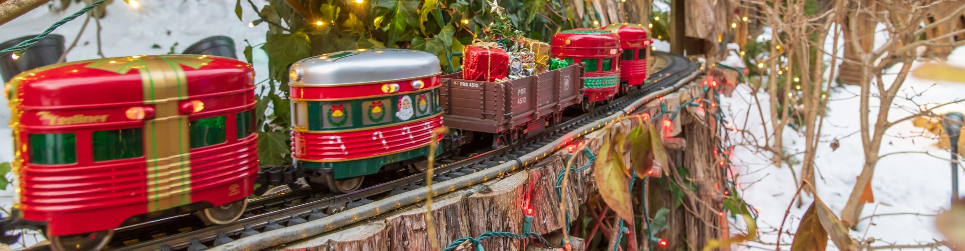An outdoor miniature train display decorated for the holidays on a snowy winter day
