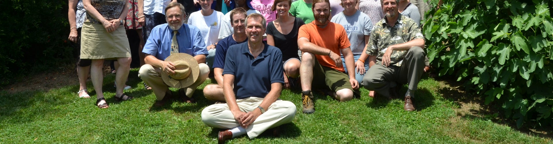 A large group of people take a staff photo in front of a building and greenery. 