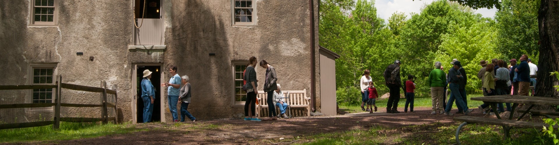 A historic mill on a sunny day with a line of people waiting to enter. 