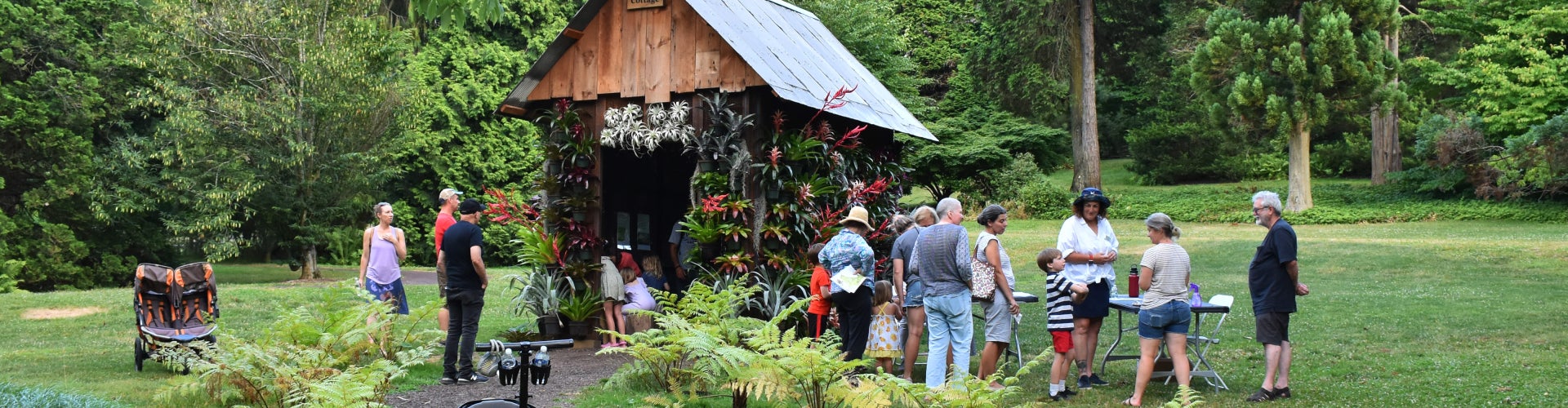 A large group of families take part in an outdoor craft activity in a public garden. 