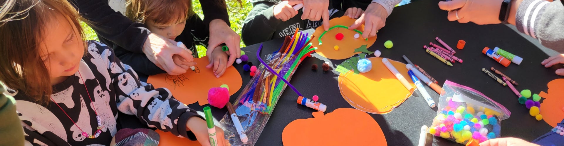 A craft able surrounded by kids and caretakers creating Halloween decorations. 