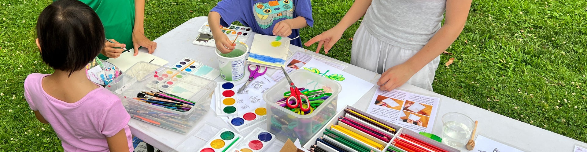 A group of children standing outside at a table making crafts. 