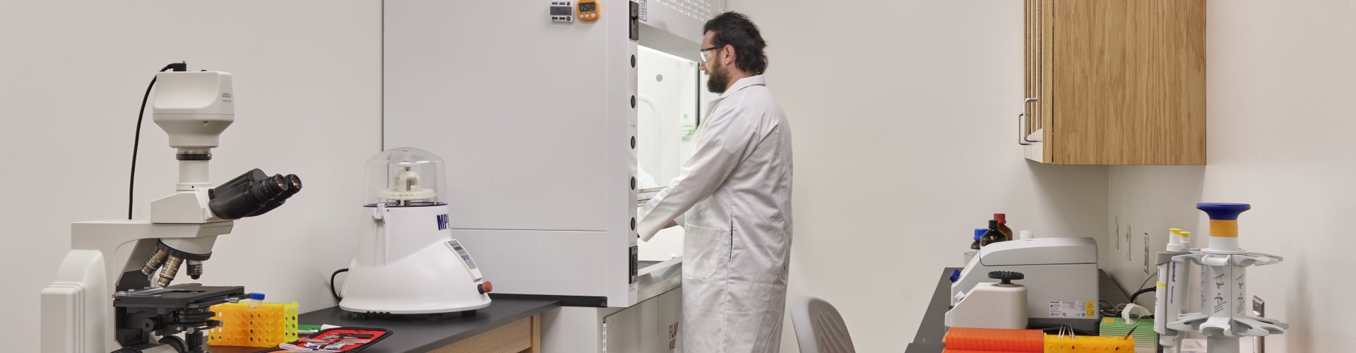A man wearing a lab coat and shoe coverings works in a laboratory.