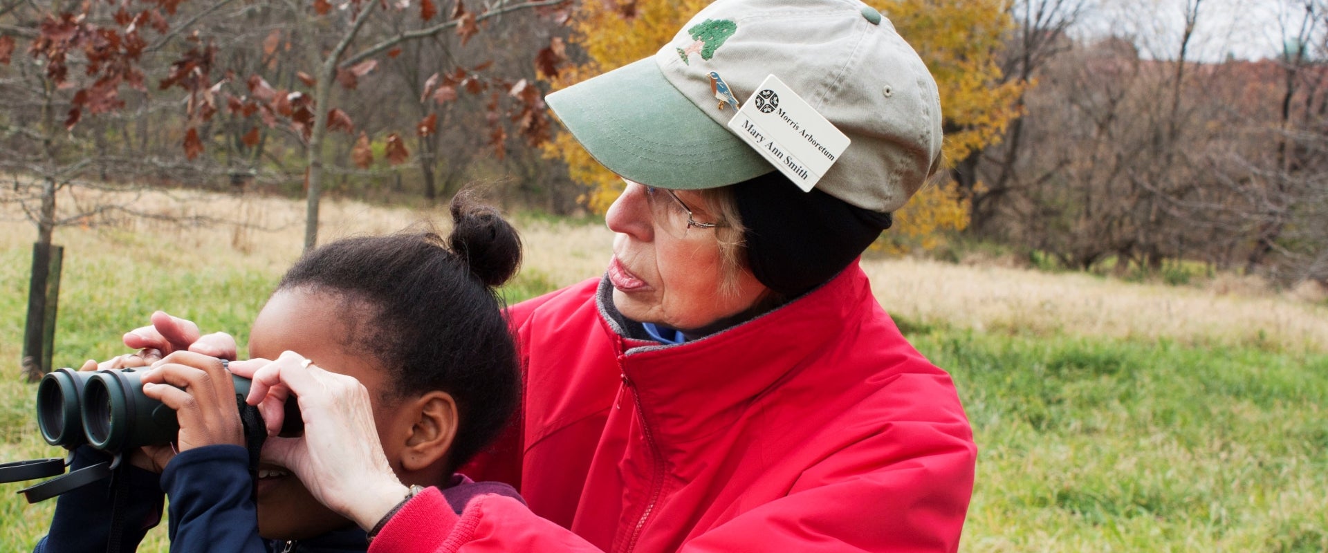 An garden volunteer shows a young girl how to use binoculars outdoors.