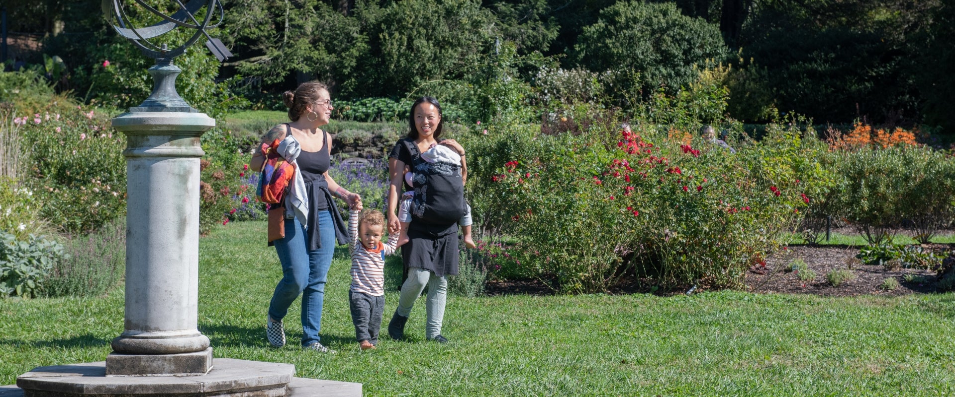 Two woman walk hand-in-hand with a child in between them through a rose garden. 