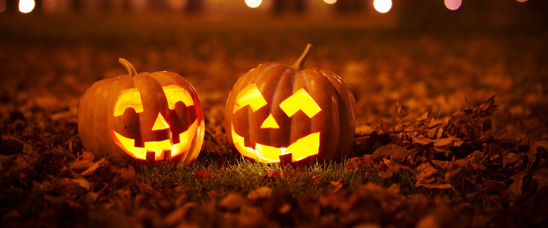 Two carved and lit up Halloween pumpkins in a patch of fallen leaves at night. 
