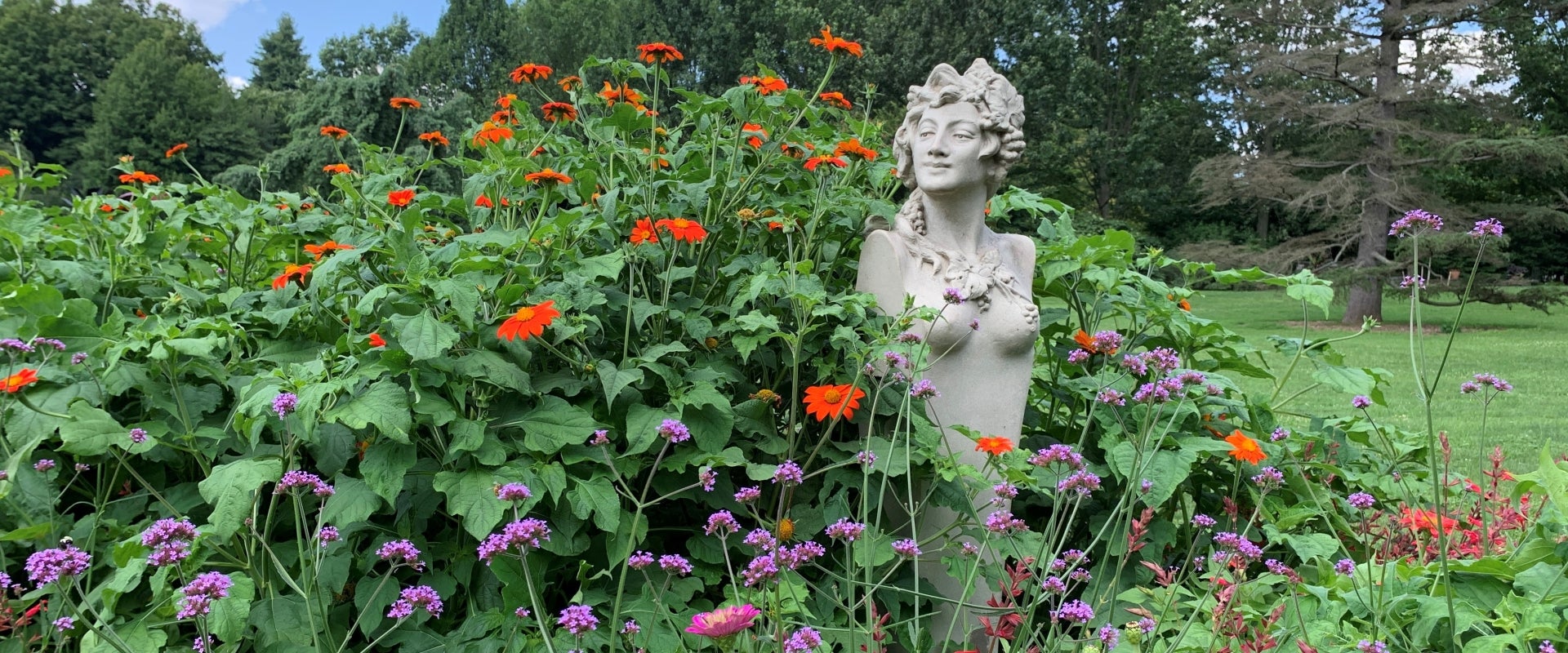 A statue of a Greek nymph among orange and purple flowers in bloom.