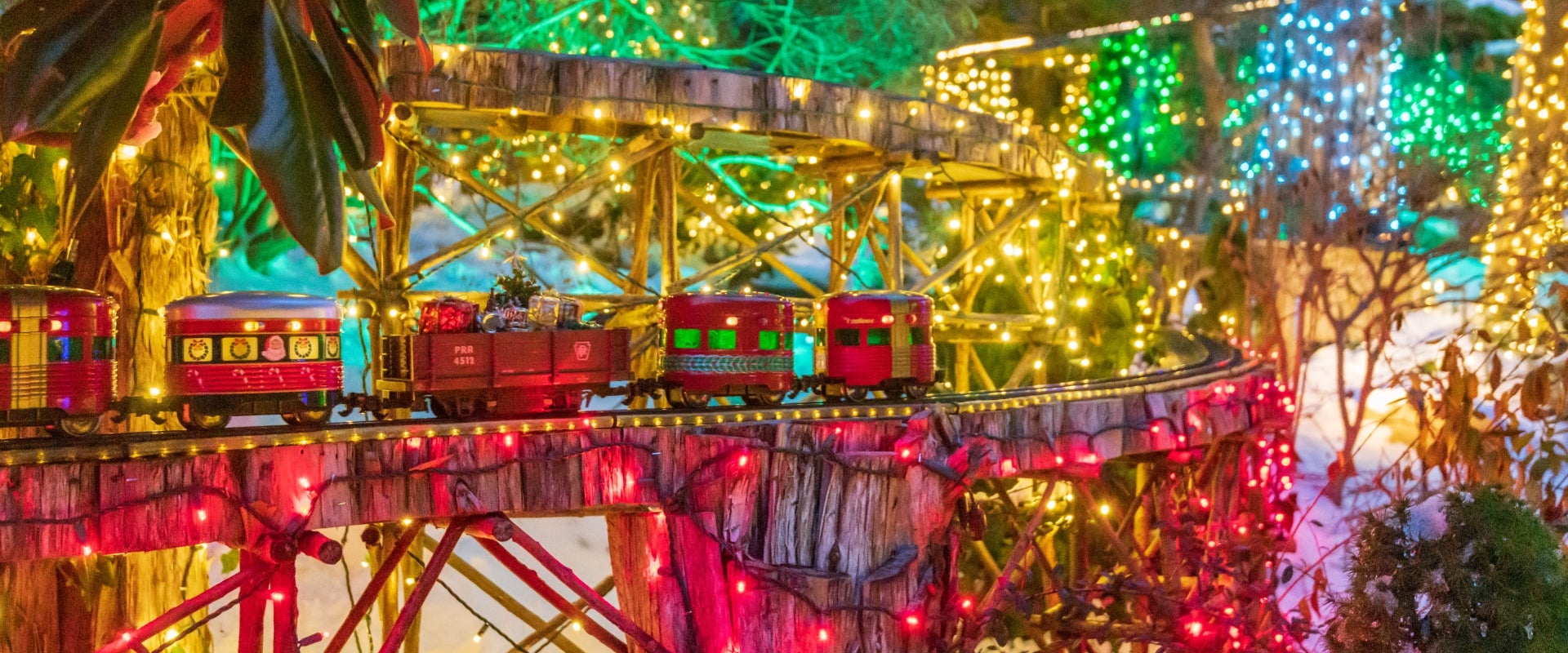 A miniature outdoor garden railway at night, decorated and lit up for Christmas. 