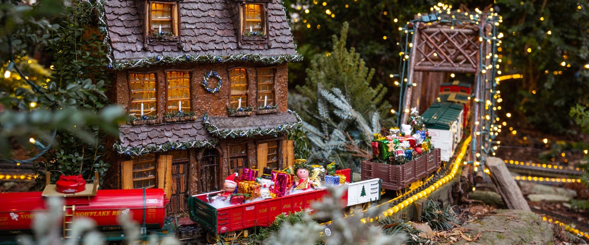 A miniature train display decorated for the holiday season with lights and other festive decor.