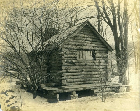 A black and white photo of a log cabin taken in the late 19th century. 