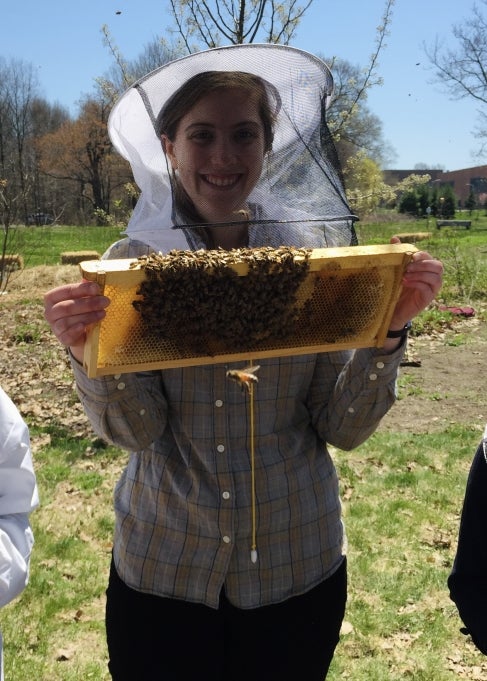 A woman in a beekeepers hat holds honeycomb covered in bees.
