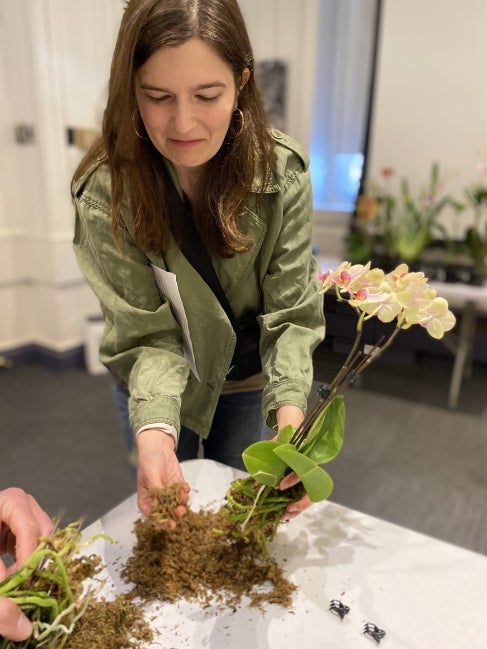 A woman holds an unpotted orchid plant in one hand and soil in the other. 