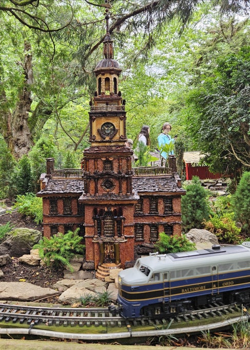 A model train rides a track around a replica of Philadelphia's Independence Hall in an outdoor garden space. 