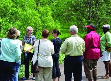A group of people on a garden tour with bright green trees in the background. 
