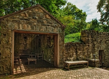 A historic springhouse made of stone with wooden furniture in a public garden.