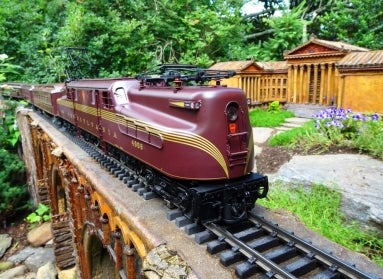  A maroon model train rides along an elevated track next to a miniature replica of the Philadelphia Art Museum.