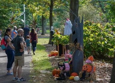 Families walking through a public garden looking at scarecrows on display. 
