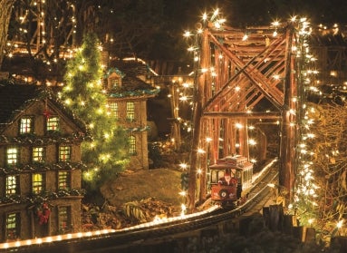 A miniature model railway at night decorated with lights and Santa riding on a train. 