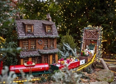 A miniature train display lit up with holiday lights and decorated for Christmas. 