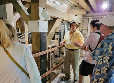 A man in a yellow shirt and tan bucket hat talks with several people.