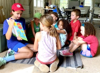 A young adult reads a story book to a group of children.