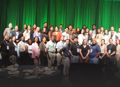 A large group of people standing on risers on a stage in front of an emerald green curtain.