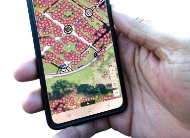 A hand holds a mobile device showing a map of a public garden. 