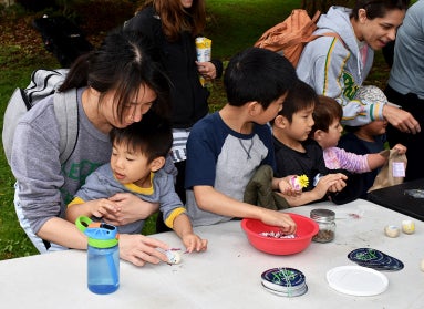A family stand at a table outdoor making crafts. 