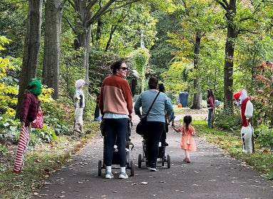 A group of people with strollers and holding children's hands walked away on a paved path lined with scarecrows.