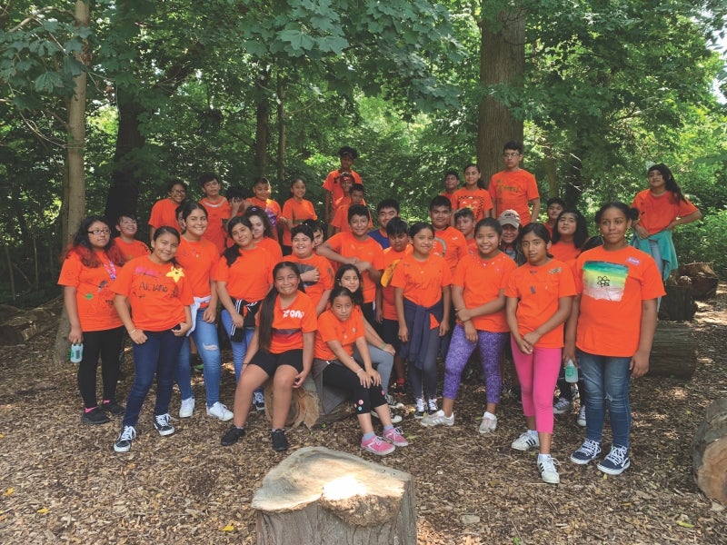 A photo of a large group of Latinx children in the woods all wearing orange ACLAMO  t-shirts