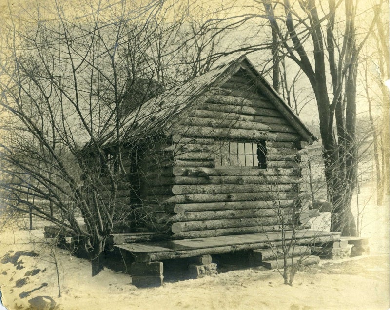 A black and white photo of a log cabin taken in the late 19th century.