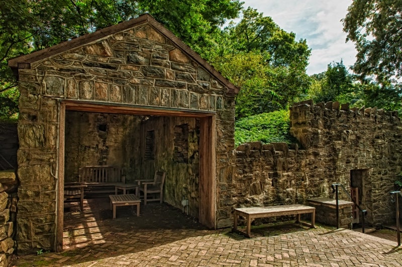 A stone springhouse with a wooden table and chair inside, surrounded by green trees. 