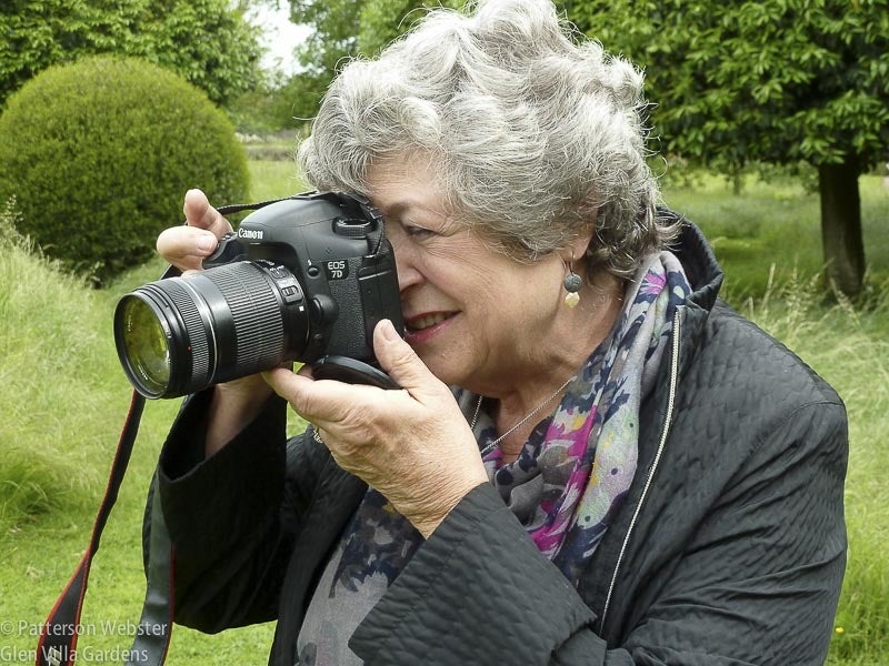 A close-up of a woman with grey hair holding a camera up to her face. 