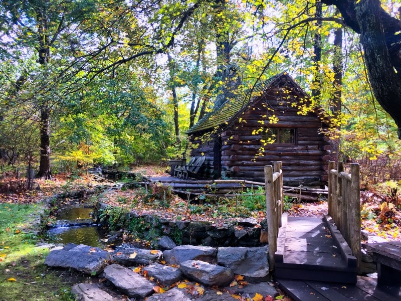 A log cabin surrounded by a creek with a wooden bridge. 