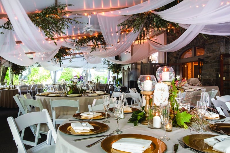 A decorated reception area with table settings, flowers, and ceiling décor. 