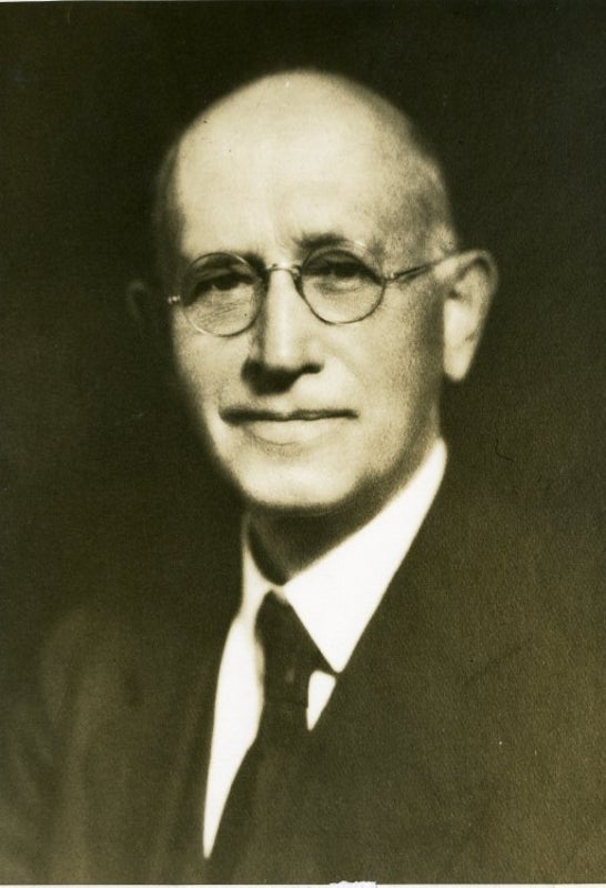 A black and white photograph of a bald man with glasses.