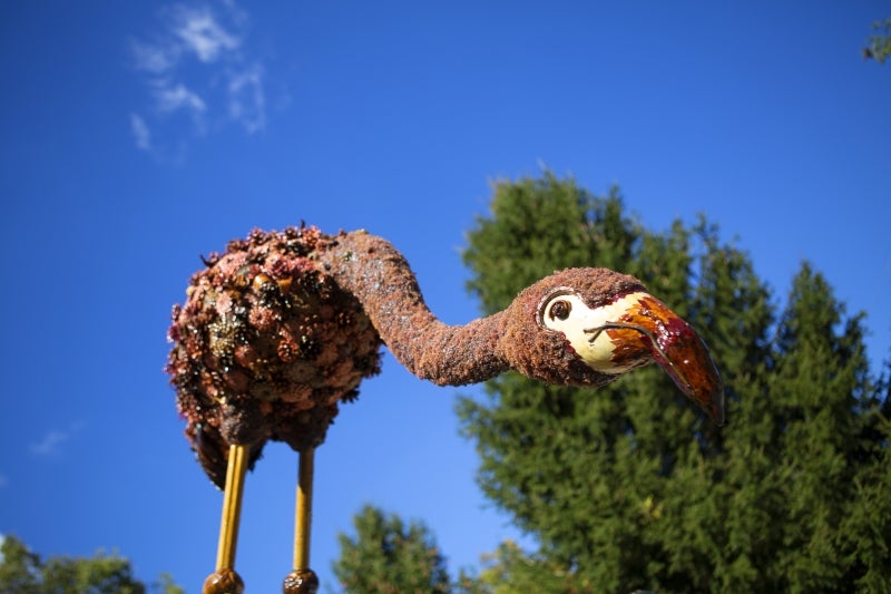 A large fabricated flamingo set against a blue sky with green trees.